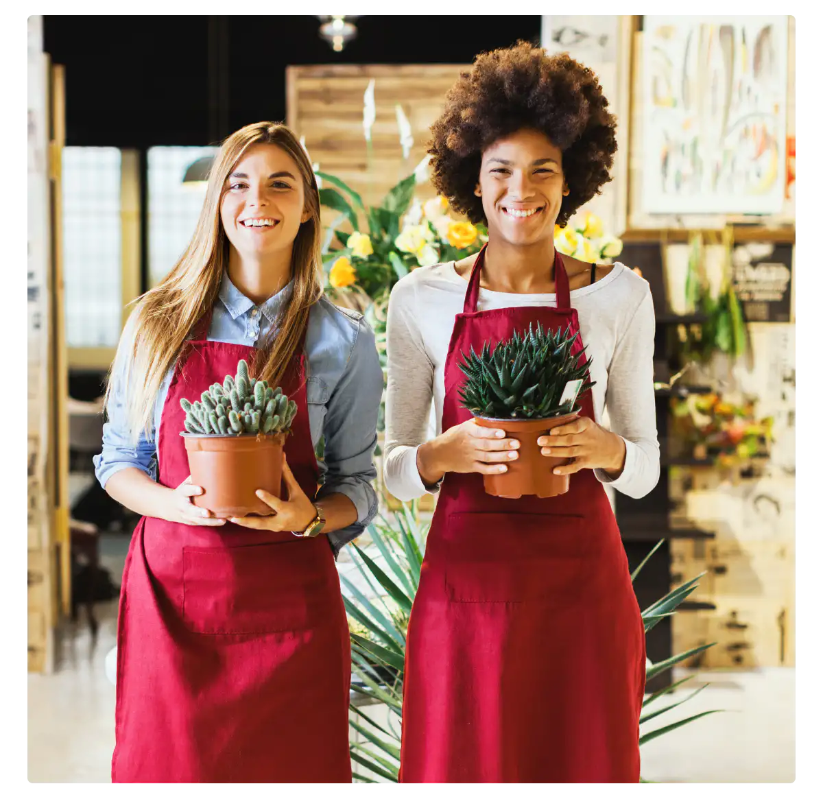 An image of smiling employees holding plants at a flower shop.